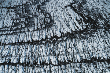 Aerial view of a glacier in Iceland showing striking natural patterns, cracks, and dark volcanic ash layers