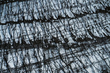 Aerial view of a glacier in Iceland showing striking natural patterns, cracks, and dark volcanic ash layers