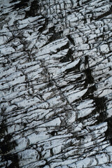 Aerial view of a glacier in Iceland showing striking natural patterns, cracks, and dark volcanic ash layers