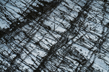 Aerial view of a glacier in Iceland showing striking natural patterns, cracks, and dark volcanic ash layers