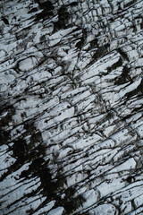 Aerial view of a glacier in Iceland showing striking natural patterns, cracks, and dark volcanic ash layers
