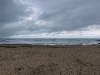 Stormy seascape with dark clouds over rough Mediterranean waves on sandy beach in Gandia Spain