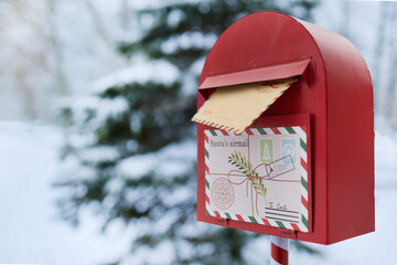 Obraz premium Santa's Mailbox. Red mailbox in snowy landscape holding a letter to Santa.