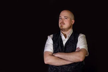Confident adult man with crossed arms wearing vest and shirt, standing against a dark background...