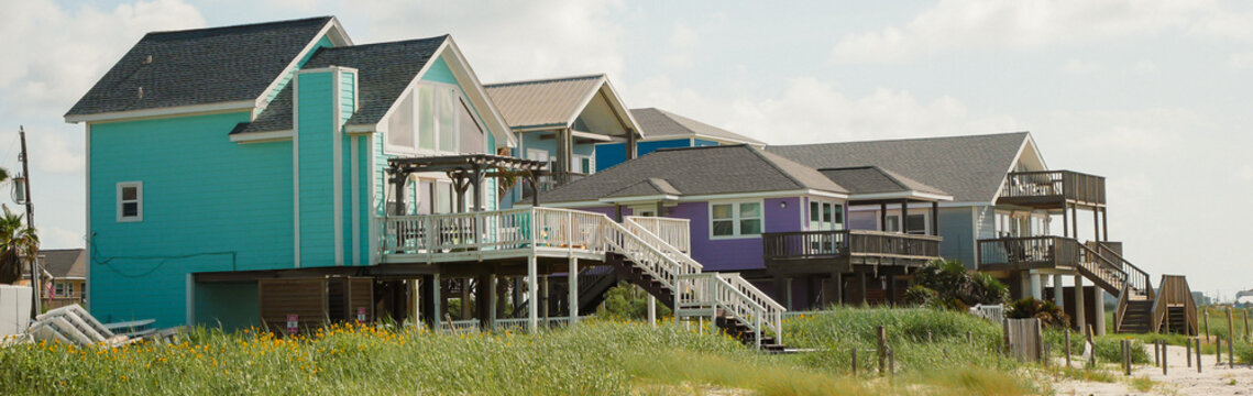 Panorama view colorful mix of stilted beach homes forms vibrant coastal cluster vacation rental, residential. Spacious balconies, elevated decks, and storm-resilient design in Galveston, TX