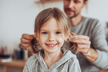 Dad gently brushing his daughter hair while she smiles happily, creating warm and loving family moment in cozy home environment