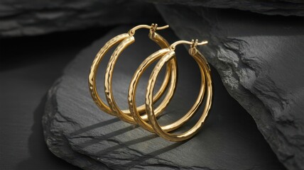 Pair of hammered gold hoop earrings displayed on dark slate stones, highlighting the texture, craftsmanship, and elegance of the minimalist luxury jewelry design