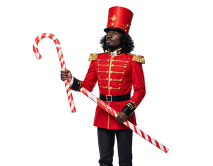 A person in a red uniform and hat holds a large candy cane against a black background