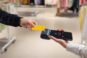 Contactless credit card payment using mobile POS terminal and smartphone in retail store, showing modern checkout process and wireless digital transaction