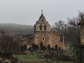 Fototapeta premium Antigua iglesia de piedra románica bajo un cielo nublado y brumoso en un entorno rural de Verdeña, Palencia, España