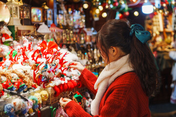 Young woman enjoying and choosing New Year's gifts in the Christmas market, surrounded by the festive decorations of the evening