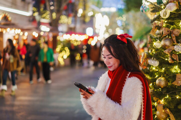 Young woman enjoying and using smartphone with the romantic Christmas market decorations at night