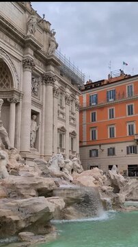 A vertical video pan from top to bottom of the magnificent Trevi Fountain in Rome, Italy, showcasing the Baroque sculptures of Oceanus, the Tritons, and the wild horses, and the turquoise water.