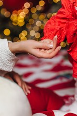 A close-up photo of a mother and daughter's hands, a child's hand, and a woman's hand against the bokeh of a Christmas tree's lights. Holiday concept.