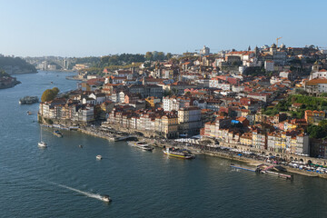 Scenic panoramic view of Porto, Portugal, with colorful historic buildings along the Douro River, traditional boats, and clear blue sky on a sunny day