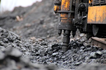 Obraz premium Close-up of a heavy drilling rig bit breaking through dark rocky ground at a construction or mining site. work