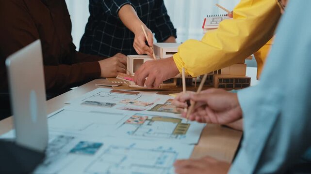 A diverse team collaborates in a modern office, engaging in discussion over detailed architectural blueprints. Hands on papers showcase creative planning and strategy. SACTR
