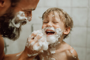Father teaching son shaving in bathroom playful moment with foam on faces happy child laughing bonding family hygiene morning routine