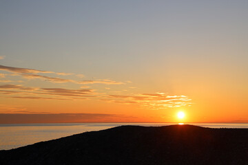 Sea waves with blue water on sand of seashore on sunset and sunrise. Yellow reflection of sunlight on surface of sea waves. Orange sky with rain clouds, horizon line and sea waves on sand. Black sea
