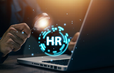 A professional uses a magnifying glass over an HR digital interface on a laptop, representing talent search, employee screening, human resources technology, and workforce management.