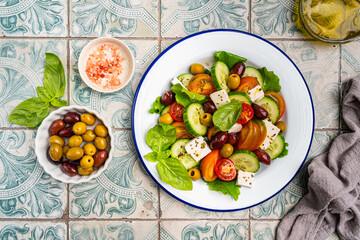 Greek salad of fresh cucumber, tomato, sweet pepper, lettuce, feta cheese and olives with olive oil on a blue tiles background. Healthy food, top view. High quality photo