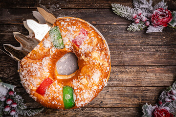 Naklejka premium Roscon de reyes with cream and christmas ornaments on a wooden background, top view. Roscon is a traditional Spanish Christmas pastry cake with decoration. Kings day concept spanish three kings cake.