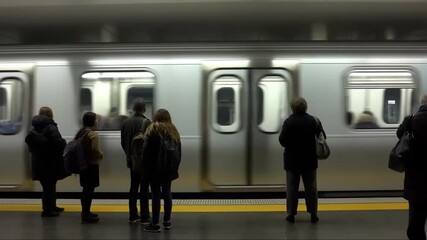 Group of commuters waiting on platform as silver subway train arrives and stops at underground station
