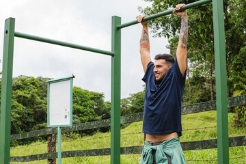 Fototapeta premium Man hanging on green bar smiling during forest workout