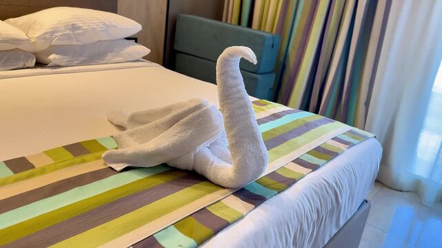A creatively folded towel swan resting on a neatly made bed, showcasing elegant craftsmanship and a touch of luxury.