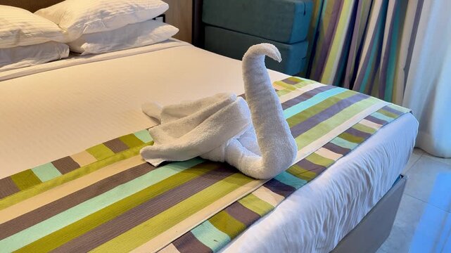 A creatively folded towel swan on a neatly made hotel bed adorned with colorful stripes.