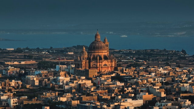 Malta, Comino island: Golden sunset over Church of Saint John the Baptist, Rotunda of Xewkija, Mediterranean Sea, traditional Maltese village landscape in peaceful evening light. Drone flight