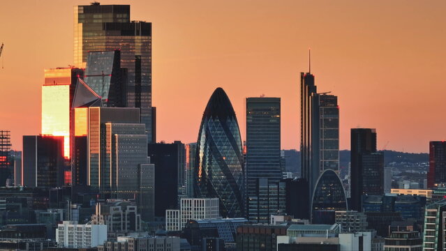 United Kingdom, London: Illuminating warm sunset colors over London's modern cityscape, highlighting iconic skyscrapers like the Gherkin in a stunning panorama. Drone flight