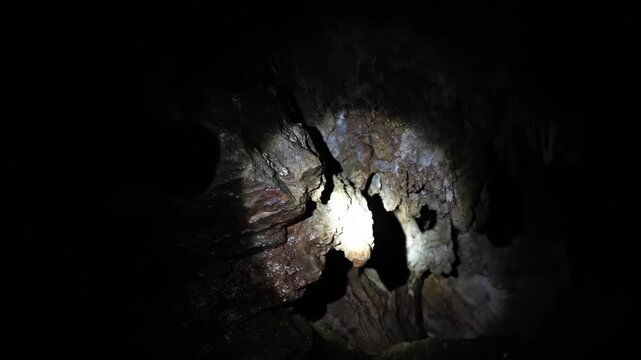 Flashlight beam scanning the walls of a dark, wet cave. First-person view of an underground exploration. Mystery and adventure concept