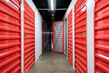 Storage corridor warehouse with open door. Self storage facility, red metal doors with locks. Moving, organizing, storage concept. Selective focus