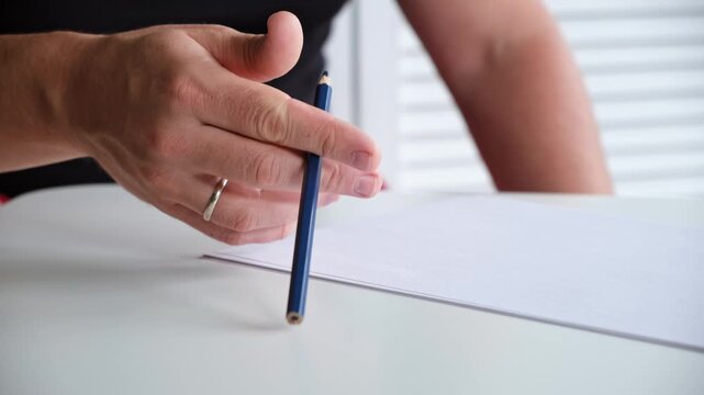 A man tapping slowly a pencil on a table with a blank sheet of paper. The concept of lack of ideas, problems, nervous state, lack of inspiration. Beat the rhythm of the melody. Music teacher. HQ 4K.
