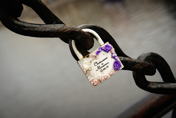 a decorative love lock attached to a heavy metal chain. Embellished love lock against blurred background. Romantic commitment. For wedding materials, romantic imagery, social media posts.