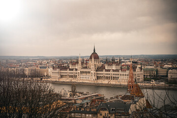 Fototapeta premium Iconic Hungarian Parliament Building in Budapest overlooking the Danube River under a moody, cloudy sky. Majestic historic architecture cityscape.