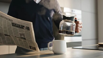 Man Pouring Coffee While Reading Newspaper - Close up of a man pouring fresh, hot coffee into a white mug while reading the newspaper. The coffee is steaming, and he appears to be in a modern kitchen.