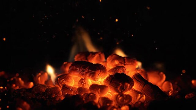 Burning Coals and Embers - The video shows glowing and burning coals with flames, set against a dark background. Sparks and embers fly upward, creating a dynamic and fiery scene.