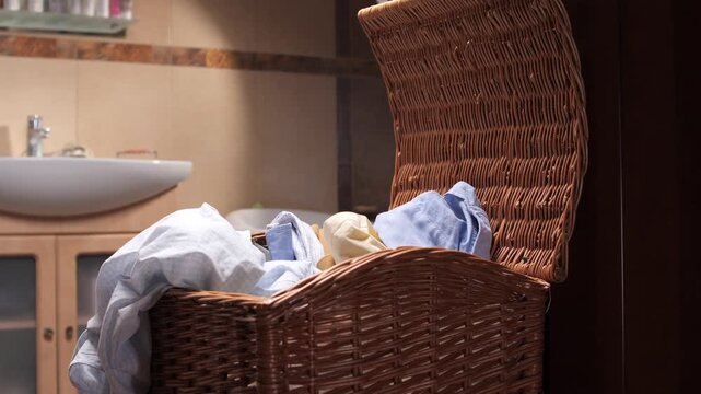 Wicker laundry basket filling with dirty clothes, showing motion blur as garments are dropped inside, creating a sense of everyday household chores and domestic life in a home bathroom