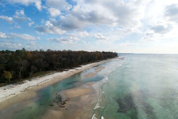 Fototapeta premium Aerial view of a serene sandy beach with clear turquoise water and lush coastal forest