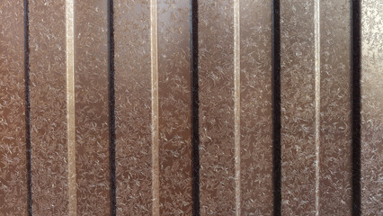 Brown frosted metal surface with vertical panels and abstract ice crystal pattern, winter texture background for design, cold season concept.