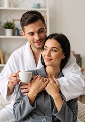 Happy young couple hugging in the morning with coffee. Man in a bathrobe embracing his smiling partner at home. Intimate romantic moment