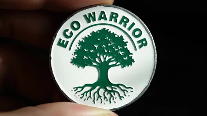 A person holds an eco warrior badge with a green tree symbol. Environmental activism and conservation concept. Close-up of a pin for climate change awareness against a black background