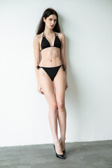 Fototapeta premium Slim fit young woman in black bikini posing in studio, healthy athletic body, minimal swimwear fashion, confident female model, beauty and fitness concept, modern clean background photography