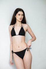 Fototapeta premium Slim fit young woman in black bikini posing in studio, healthy athletic body, minimal swimwear fashion, confident female model, beauty and fitness concept, modern clean background photography