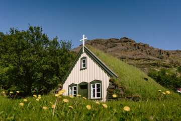 A small turf church surrounded by green grass and mountains in Iceland