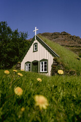 A small turf church surrounded by green grass and mountains in Iceland