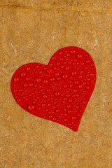 wet hard yellow cardboard for packaging goods and products with red plastic hearts glued on , a piece of corrugated cardboard with heart covered with water droplets