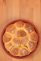 An overhead shot of sweet dough buns, golden brown and sprinkled with sugar, arranged in a red round baking mold on a wooden surface